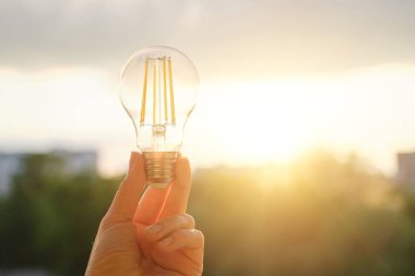 Filament led ampuller, el tutma lambası, akşam gün batımı gökyüzü arka plan