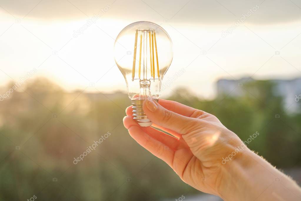 Filament led lightbulbs, hand holding lamp, evening sunset sky background