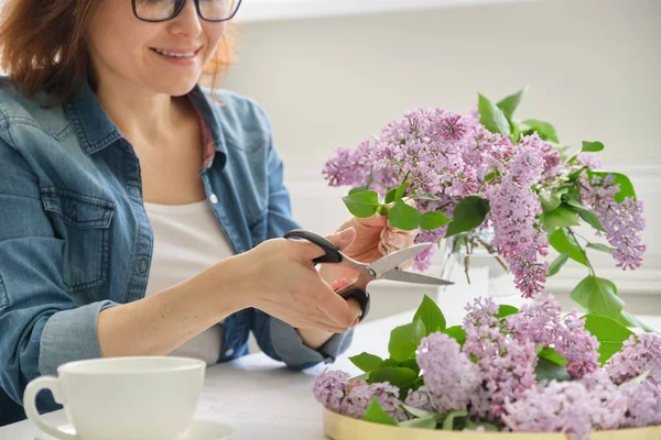 Olgun kadın masada evde leylak dalları buket yapma