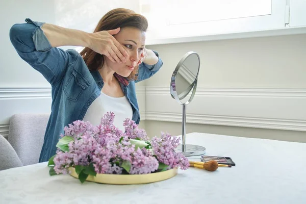 Portret van volwassen vrouw met make-up spiegel masserende haar gezicht en nek, mooie vrouwelijke 40 jaar oud — Stockfoto