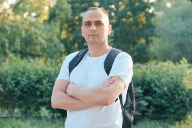 Kendine güvenen orta yaşlı spor adamının açık hava portresi. Kolları beyaz tişörtle kameraya bakan yakışıklı erkek