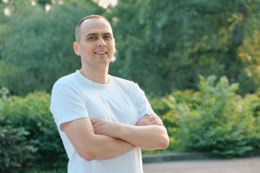 Kendine güvenen orta yaşlı spor adamının açık hava portresi. Kolları beyaz t-shirt kameraya bakarak geçti pozitif yakışıklı erkek