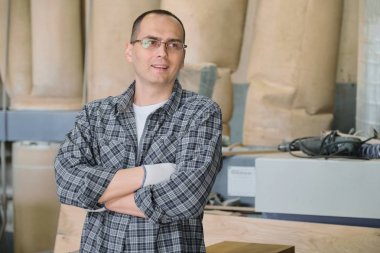 Endüstriyel üretimde erkek işçi portresi. Çapraz kollu rahat gömlek gözlük eldiven kendinden emin adam.