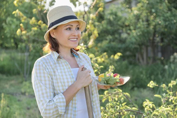 Retrato al aire libre de mujer madura positiva en sombrero de paja. Sonriente hembra con plato de fresas menta limón, fondo verde jardín, día soleado puesta de sol — Foto de Stock