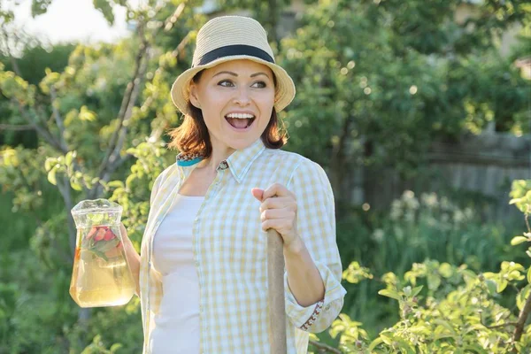 Leende kvinna med kanna av uppfriskande naturlig hemlagad dryck i sommar trädgården — Stockfoto