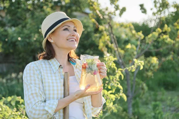 Retrato de mujer feliz madura en sombrero en el jardín con bebida herbal casera natural con fresas de menta — Foto de Stock