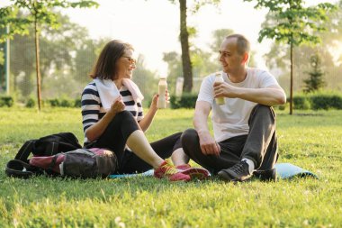 Fitness minyonu üzerinde parkta oturan mutlu olgun çift, spor egzersizleri sonra yoğurt içme dinlenme.