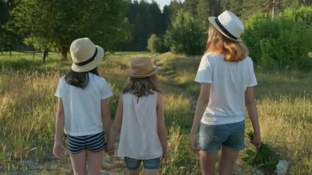 Дети три девушки в шляпах, держась за руки, возвращаются по сельской дороге — стоковое видео