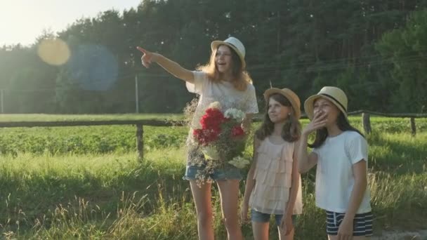 Tres niñas niños con ramo de flores muestran el dedo en el camino, emociones alegría y felicidad, esperar y conocer — Vídeos de Stock
