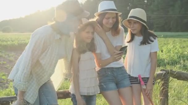 Madre feliz con tres hijas mirando al teléfono inteligente, familia en la naturaleza — Vídeo de stock