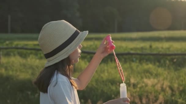 Красивая девочка в шляпе, надувающая мыльные пузыри — стоковое видео