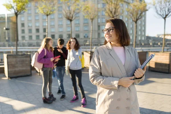 Портрет взрослой улыбающейся учительницы в очках с планшетом, на открытом воздухе с группой подростков — стоковое фото