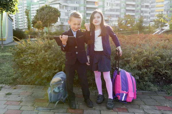 Chłopiec i dziewczynka w szkole podstawowej z cyfrowym tabletem. Tło na zewnątrz, dzieci z torbami szkolnych, spójrz na tablet. — Zdjęcie stockowe