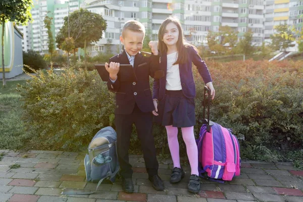 Alunos de meninos e meninas na escola primária com tablet digital. Fundo ao ar livre, crianças com bolsas escolares, olhar para o tablet . — Fotografia de Stock