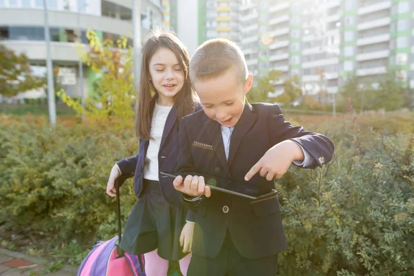 Хлопчик і дівчинка в початковій школі з цифровим планшетом. На відкритому повітрі, діти зі шкільними сумками, дивіться на планшет . — стокове фото