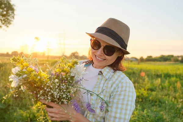 Mogen kvinna med blommor i en sommaräng, gyllene timmen — Stockfoto