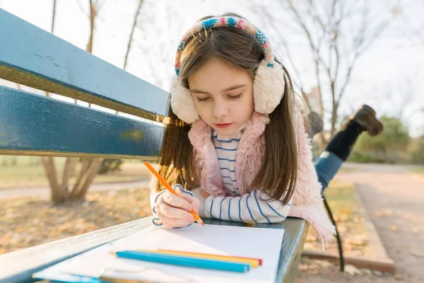 Desenho bonito pequeno do artista com lápis coloridos, menina que senta-se em um banco no parque ensolarado do outono — Fotografia de Stock