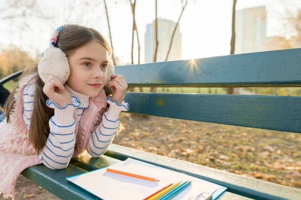 Piccolo bellissimo artista disegno con matite colorate, ragazza seduta su una panchina nel soleggiato parco autunnale — Foto Stock