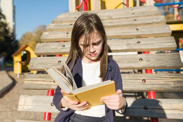 Buiten portret van beledigd klein meisje. Kind lezen boek, offendedly pouting haar lippen. — Stockfoto