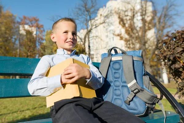 Ragazzino 6,7 anni con libro. Ritratto di bambino con libro grande, lettura e seduta su panchina — Foto Stock