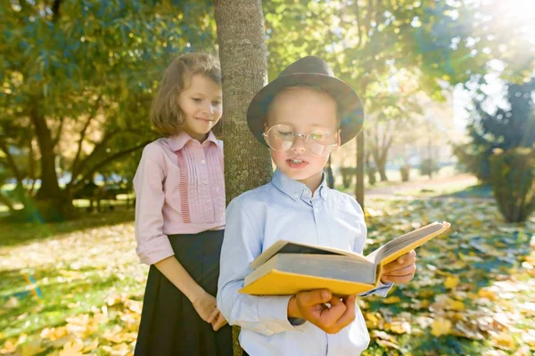 Niño pequeño 6,7 años con sombrero, gafas, libro de lectura y niña 7,8 años —  Fotos de Stock