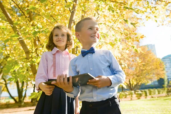 Két gyerek nézi a digitális tabletta, a háttérben őszi Sunny Park — Stock Fotó