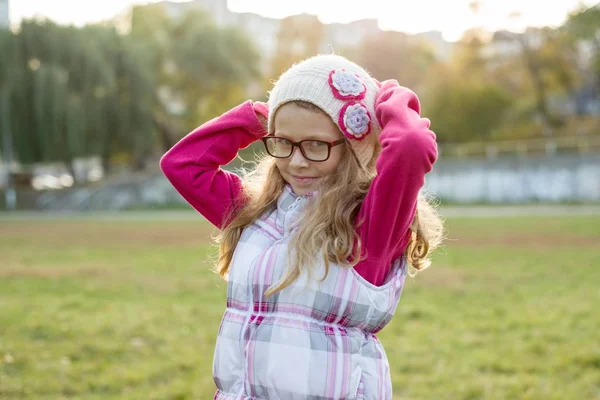 Porträtt av en lycklig flicka 7 år gammal, i en Stickad mössa, Glasögon, höst solig bakgrund — Stockfoto