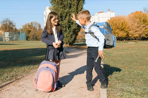Мальчик и девочка, ученики начальной школы с рюкзаками ходят в школу. Солнечный день фон, дорога в парке — стоковое фото