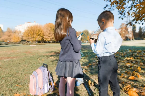 Buiten portret van jongen en meisje leerlingen in de lagere school. Kinderen in hoofdtelefoons met mobiele telefoons — Stockfoto