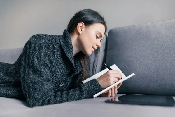 Portrait d'automne d'hiver d'une jeune fille dans un pull chaud tricoté à la maison sur le canapé avec une tablette numérique et un cahier — Photo