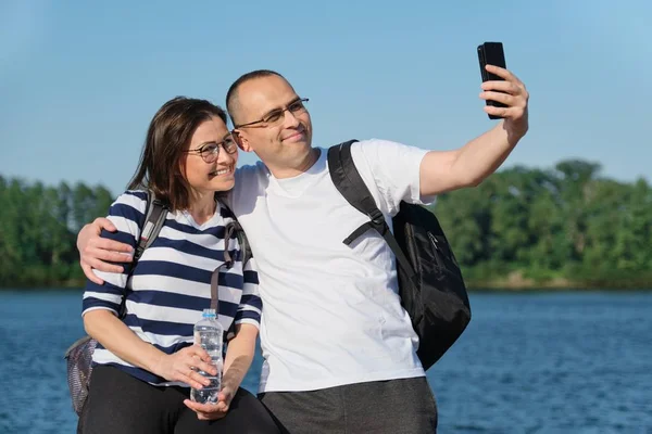 Érett boldog pár figyelembe selfie fotó telefonon, az emberek pihentető közelében folyó nyári esti parkban — Stock Fotó
