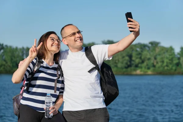 Érett boldog pár figyelembe selfie fotó telefonon, az emberek pihentető közelében folyó nyári esti parkban — Stock Fotó