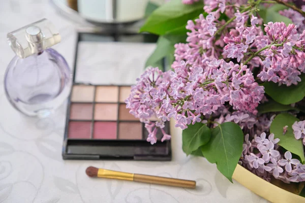 Maquillaje decorativo cosméticos, botella de perfume, sombra de ojos, flores de color lila fresco —  Fotos de Stock