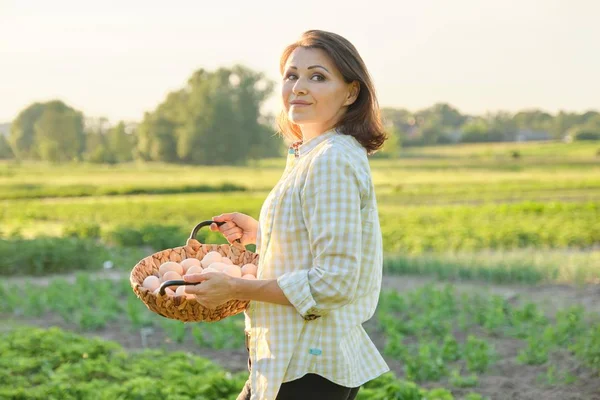 Utomhus porträtt av bonde kvinna med korg av färska kyckling ägg, gård — Stockfoto