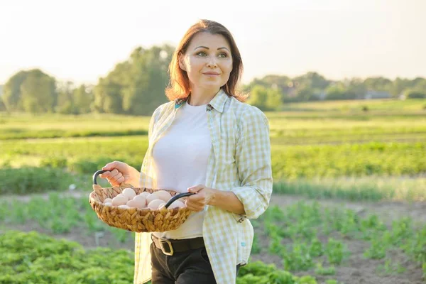 Utomhus porträtt av bonde kvinna med korg av färska kyckling ägg, gård — Stockfoto