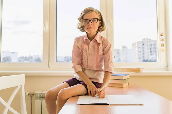 Colegiala, niña de 8 años, sentada a la mesa con libros —  Fotos de Stock