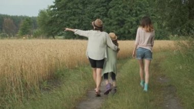  Aile Anne ve çocuklar iki kız birlikte ülke yolu boyunca yürüyüş, arka görünüm, yaz doğa arka plan, buğday alanı, altın saat