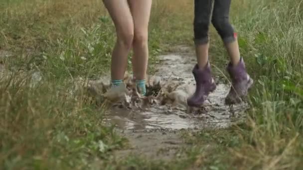 Nohy dvou dětí v botách skáčou v deštivé malé kaluži — Stock video