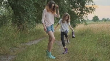 Kirli giysiler içinde yağmurdan sonra yürüyen iki mutlu kız kardeş botlarından su dökerken eğleniyor