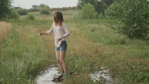 Hermosa chica adolescente sonriente saltando en un charco muy fangoso — Vídeo de stock