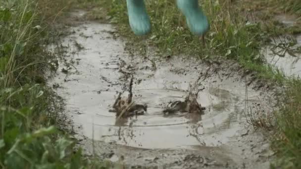 Gros plan des jambes des filles en bottes sautant dans une flaque d'eau très boueuse — Video