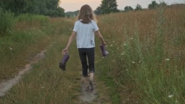 Elinde botlarla kırsal yolda yürüyen kız