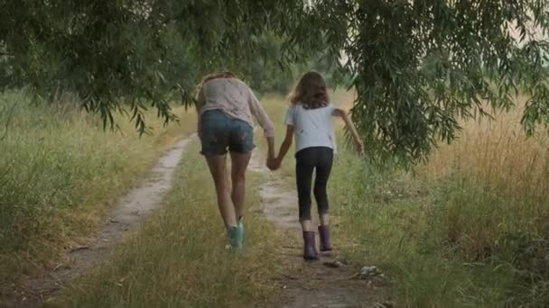 Duas irmãs meninas felizes andando após a chuva em roupas sujas segurando as mãos para trás vista — Vídeo de Stock