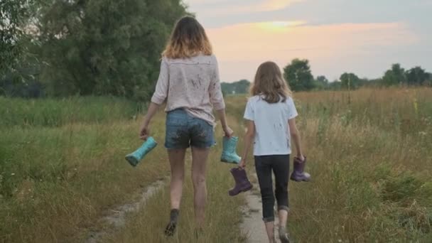 Due sorelle ragazze felici che camminano dopo la pioggia in vestiti sporchi vista posteriore — Video Stock