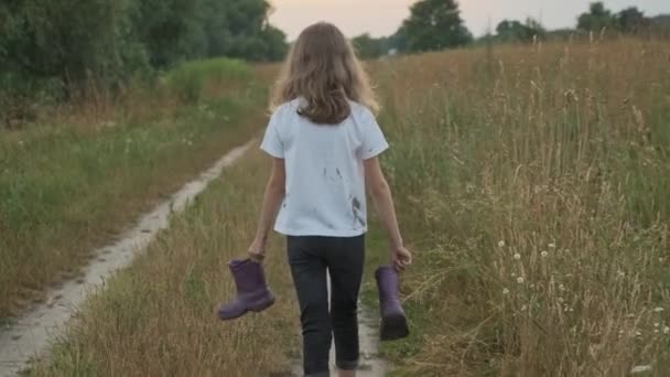 Κορίτσι περπατάει σε αγροτικό δρόμο με μπότες στα χέρια της — Αρχείο Βίντεο