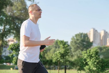 Gözlüklü orta yaşlı erkek kulaklıkile şehir parkı ile çalışır