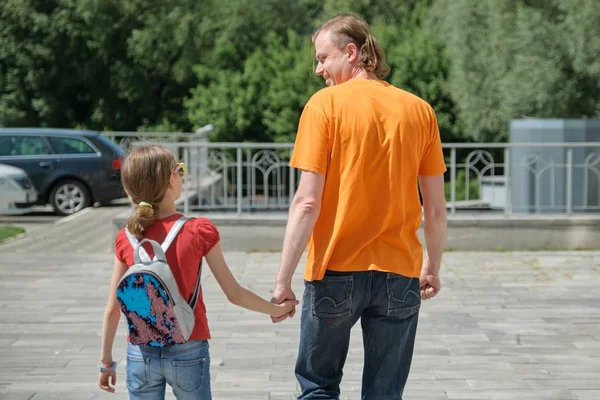 Papá camina con su hija cogida de la mano. Al aire libre, día de verano soleado, vista trasera — Foto de Stock