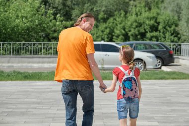 Babam kızıyla el ele yürüyor. Açık, güneşli yaz günü, arka görünüm