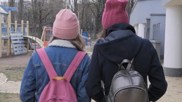 2人の歩く女の子 コート バックパック付きジャケット バックビュー 春の冬の秋の季節 屋外でティーンエイジャー — ストック動画