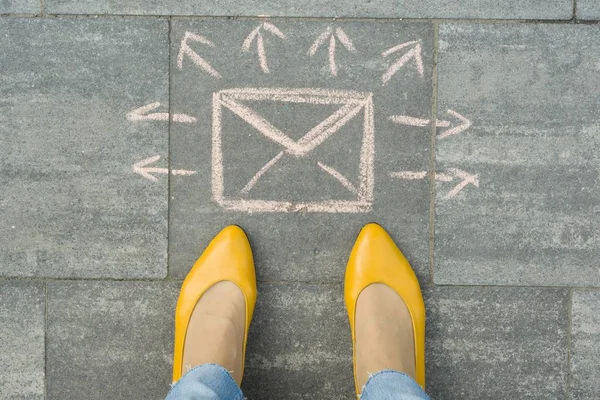 Female feet with abstract envelope message letter with arrows in different directions, written on grey sidewalk — Stock Photo, Image